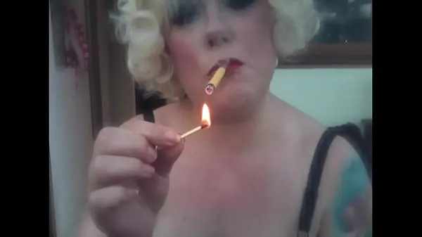 Afficher Une maîtresse rétro blonde fumant une cigarette Sobranie jaune avec une lumière d'allumettemes clips